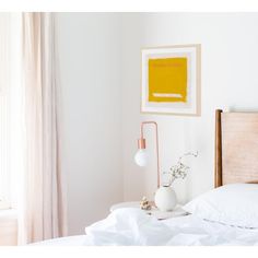 a bed with white sheets and a painting on the wall above it, next to a lamp