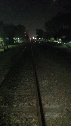 a train track at night with the lights on and trees in the backround