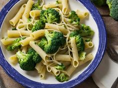 a blue and white bowl filled with pasta and broccoli on top of a wooden table