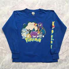 a blue long sleeved shirt with pokemon characters on the front and back, sitting on a white surface