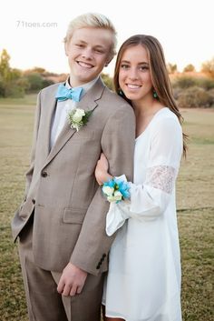 a young man and woman standing next to each other in front of an open field