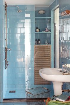 a blue tiled bathroom with a sink, shower and shelves on the wall above it