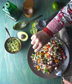 a person holding a plate of food with avocado and salsa on the side