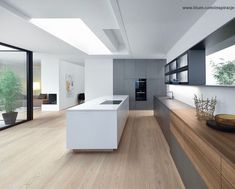 a modern kitchen with wood flooring and white counter tops, along with large windows