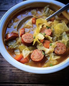 a bowl of cabbage and sausage soup with a spoon in it on a wooden table