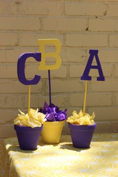 two purple and yellow cups with flowers in them sitting on a table next to a brick wall