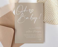 a baby announcement card on top of some brown envelopes next to a straw hat