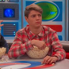 two young men sitting at a table with popcorn in front of them and one holding his hand out