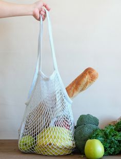 a person holding a bag full of food next to some vegetables and an apple on a table