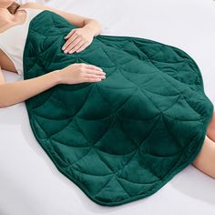 a woman laying on top of a bed under a green blanket