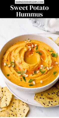 sweet potato hummus in a white bowl surrounded by crackers and tortilla chips