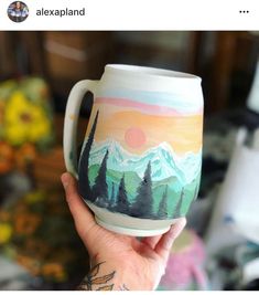 a person holding up a coffee mug with mountains and trees painted on the inside of it