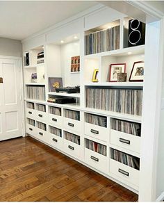 there is a large white bookcase with many records on it in the room that has wood flooring