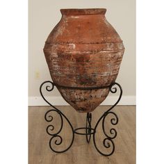 an old urn sitting on top of a metal stand in front of a wall