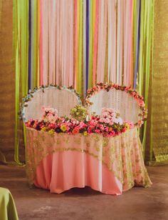 two round tables with flowers on them in front of colorful draping and curtains