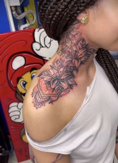 a woman with braids has a tattoo on her neck and shoulder, while she is looking at the camera