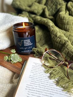 an open book with glasses on it next to a candle and eyeglasses sitting on a blanket