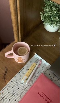 a cup of coffee next to a pink notebook