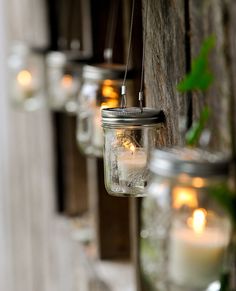 mason jars hanging from the side of a wooden fence filled with candles and greenery