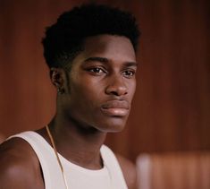 a young man in a white tank top and gold necklace looking at the camera with an intense look on his face