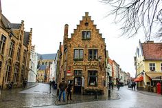 some people are walking down the street in an old european town on a rainy day