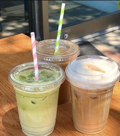 two drinks are sitting on a table next to each other with straws in them