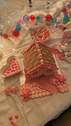 a table topped with lots of pink and white candies next to a gingerbread house