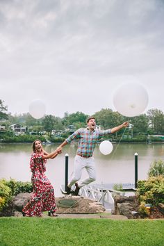 a man and woman holding balloons in front of a lake