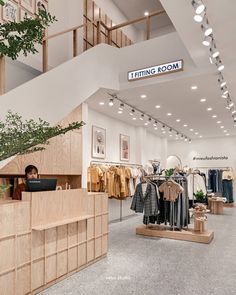 a woman is sitting at a desk in a clothing store with clothes hanging on the walls