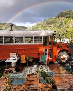 an orange bus parked on top of a wooden deck next to a rainbow in the sky