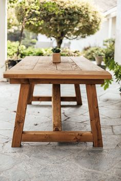 a wooden table sitting on top of a stone floor next to a potted plant