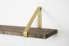 a wooden shelf with gold metal brackets on the top and bottom, against a white wall