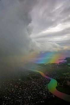 a rainbow appears in the sky over a river and cityscape as seen from an airplane