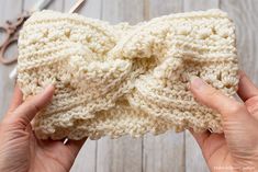 two hands holding up a crocheted bow on top of a wooden table next to scissors