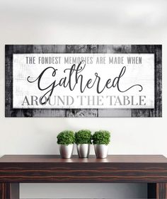 a wooden table with three potted plants on it and a framed sign above it