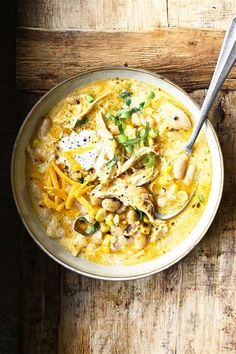 a white bowl filled with food on top of a wooden table next to a spoon