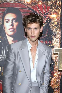 a man in a gray suit standing next to a wall with a movie poster on it