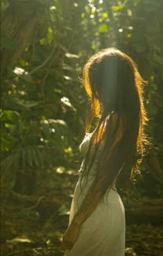 a woman with long hair standing in the woods