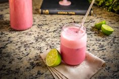 a pink drink sitting on top of a counter next to two limeades and a book