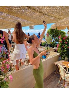 a woman in a green dress is holding an umbrella and taking a selfie with her cell phone