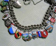 "Loaded Vintage 800 Sterling Silver Enamel European Travel Shield Charm Bracelet, Silver Souvenir Travel Bracelet, Old Charm Bracelet A beautiful vintage silver and enamel travel shield charm bracelet.  All of the charms are European in origin and there are 35 in all.  The bracelet measures approximately 6 3/4\" long with the charms measuring approximately 7/16\" wide.  The majority of the charms are 800 silver, a couple of them are sterling and a couple are not marked.  The bracelet is marked with a lion passant which means it is sterling.  The clasp is a heart padlock and the bracelet has a safety chain.  Overall, the condition is good.  A couple of the enamel charms have some slight enamel loss. Scotland, London, Denmark, Holland, Berlin, Munchen, Salzburg, Wien, Heidelberg, Atomium, In Travel Bracelet, Heart Padlocks, Safety Chain, Enamel Charms, Silver Enamel, European Travel, Vintage Silver, Jewelry Bracelets, Charm Bracelet