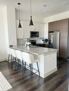 a kitchen with white cabinets and marble counter tops, an island in the middle is surrounded by bar stools