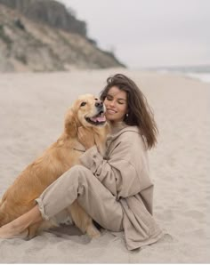 a woman is sitting on the beach with her golden retriever, who is hugging her face