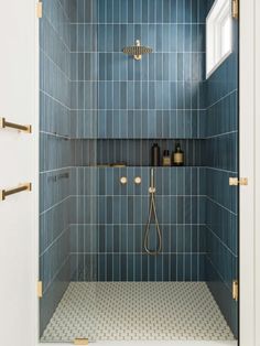 a blue tiled shower with gold fixtures and hand held shower head in the corner,