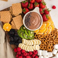 a platter with fruit, pretzels, crackers and dip