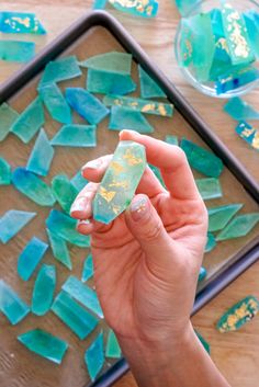 a person holding a piece of glass in front of some blue and gold pieces on a tray