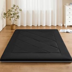 a black mat on the floor in front of a window with white curtains and a potted plant