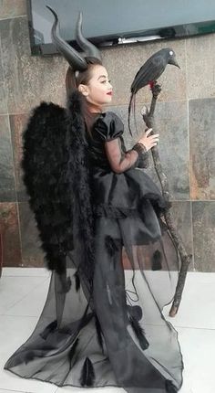 a woman dressed in black with horns and wings is holding a bird on her arm