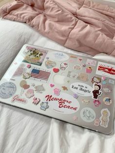 an open laptop computer sitting on top of a bed covered in pink sheets and stickers