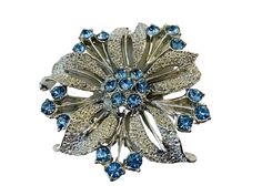 This Vintage Costume Flower Brooch in Silver Tone with Blue Stones is a stunning piece of vintage jewelry that is sure to turn heads. The brooch is beautifully crafted with intricate detailing, featuring a lovely flower design that is both elegant and timeless. The blue stones add a pop of colour and sparkle, creating a beautiful contrast against the silver tone metal. The brooch is in excellent vintage condition and is a perfect accessory to add to your collection. It can be worn on a coat, jacket, or even as a statement piece on a scarf or hat. The beauty and craftsmanship of this vintage brooch make it a wonderful gift for someone special or a great addition to your own jewelry collection.  Dimensions: W- 4.5cm For More Great Items:  The Vintage Crate:  Located in Arnprior, Ontario, ser Flower Shaped Costume Jewelry Brooches For Wedding, Blue Flower Brooch With Floral Decoration, Blue Flower Brooches With Flower Decoration, Blue Floral Brooch Jewelry, Blue Flower-shaped Jewelry Brooch, Blue Flower Brooch For Wedding, Formal Blue Flower Brooch, Formal Blue Flower Brooches, Vintage Crate